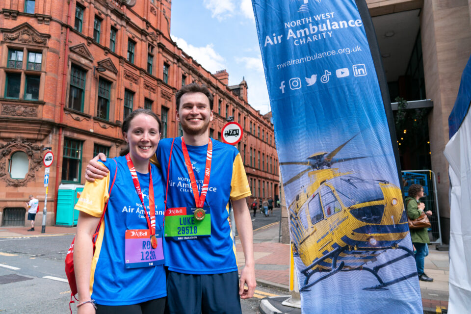 Woman and man standing smiling next to North West Air Ambulance banner