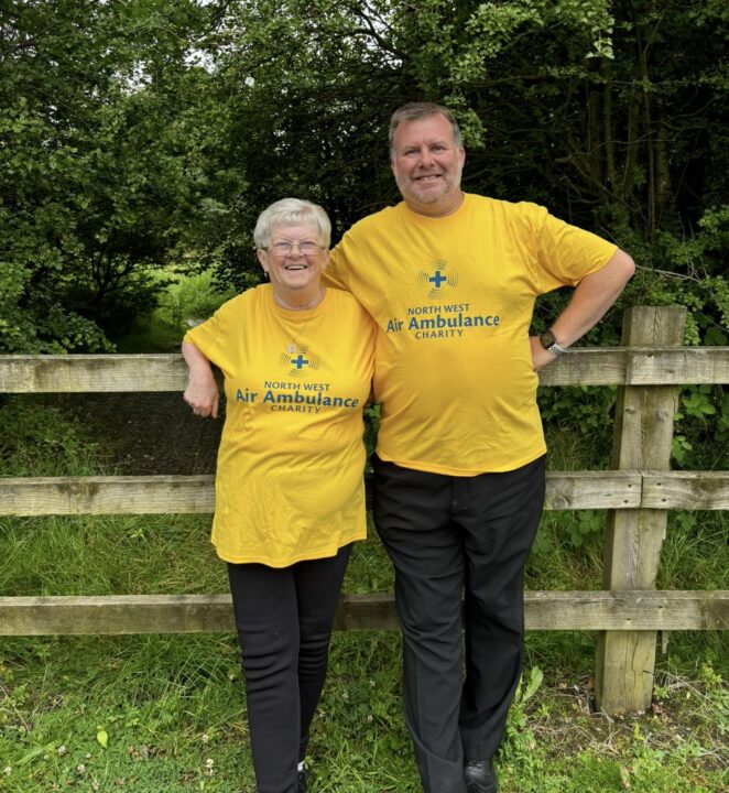 Man and woman stood in front of a fence wearing NWAA yellow fundraising tee shirts