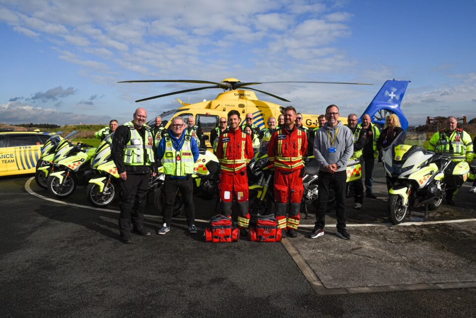 Crew at NWAA and Blood bike team stood in front of yellow helicopter