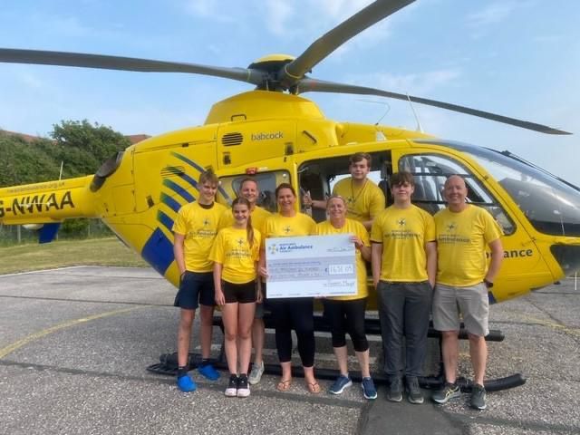 Group of fundraisers stood in front of the charity's yellow helicopter with a cheque 