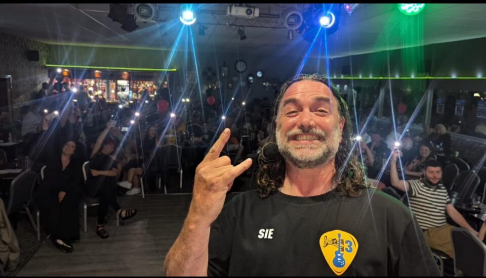 Man stood on stage taking a selfie with a crowd in the background at music night Gazjam