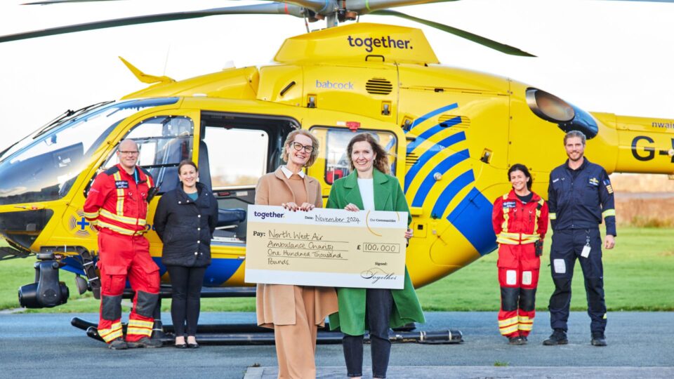 CEO Heather Arrowsmith with Together presenting a cheque in front of the charity's helicopters